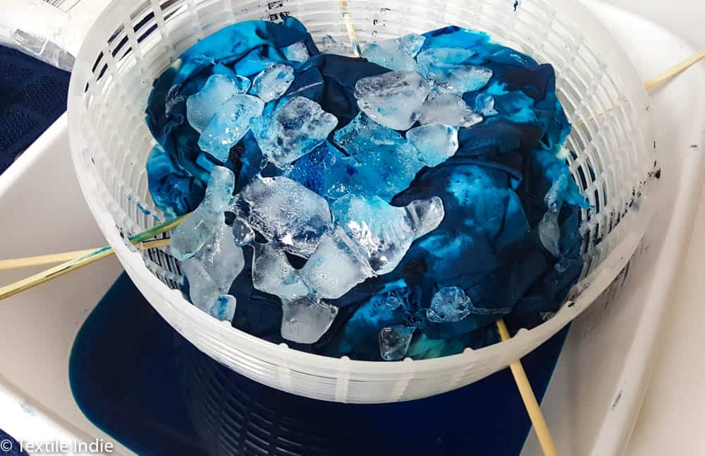 Ice cubes almost completely melted in a bowl of ice dyed fabric.