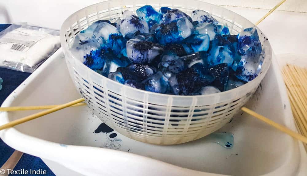 Ice cubes covered in dye sitting on top of cotton fabric for the ice dyeing process.
