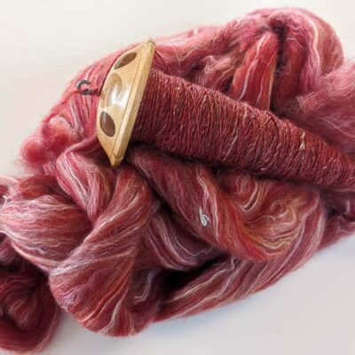 pink wool roving with a wooden drop spindle sitting on top