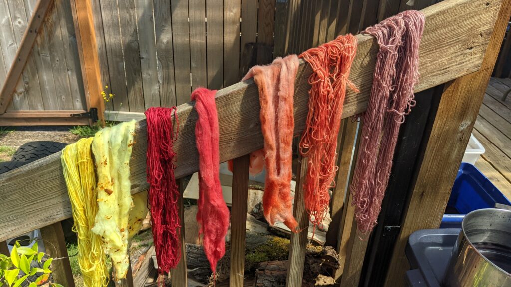 fiber in reds, oranges, and yellows drying over a deck railing