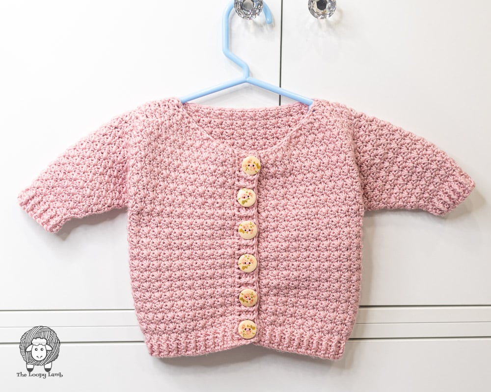 pink crochet baby sweater with buttons on a blue hanger 