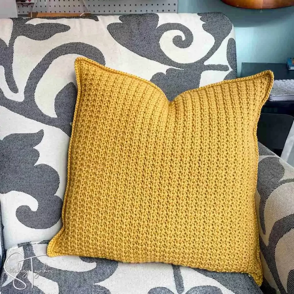 gold textured crochet pillow on a grey and white chair
