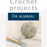Ball of grey yarn attached to a blue metal crochet hook. Two more crochet hooks sit in the foreground.