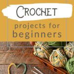 Balls of yarn in greens and golds on a wooden table, a heart has been chain stitched.