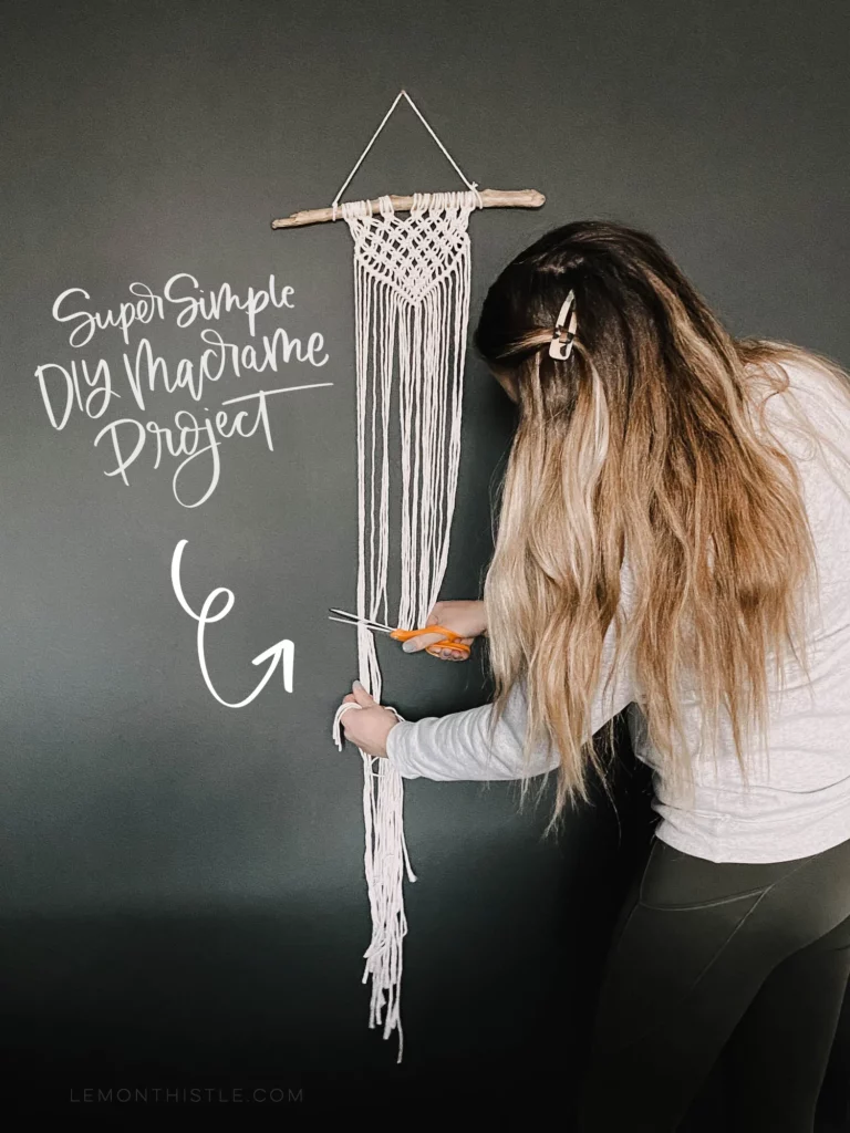 Woman cutting the ends of a macrame wall hanging, she's wearing a white shirt and gray yoga pants