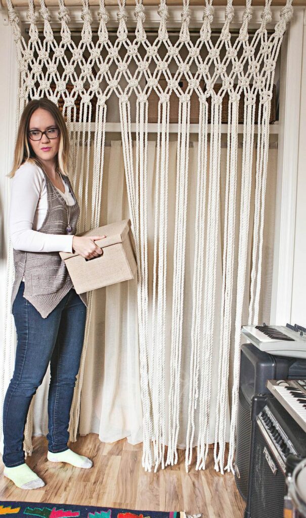 Woman holding a storage box is standing next to a beautiful macrame closet curtain 
