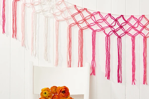 Delicate and lacy macrame wall hanging is done in hues of pink from light shell pink to fuchsia 