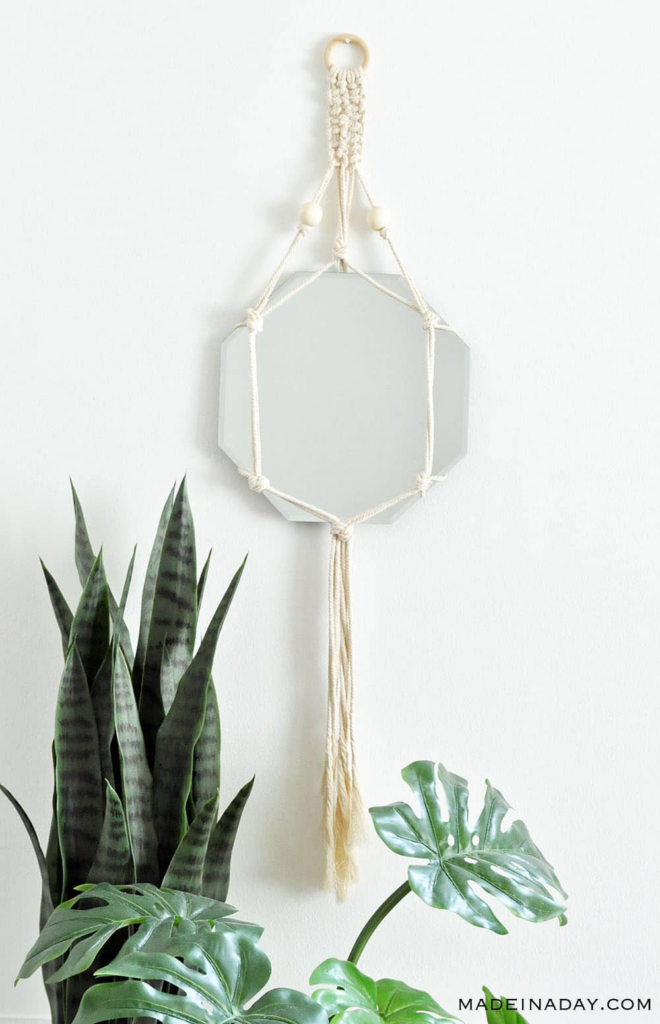 A macrame wall hanging holds an octagonal mirror. There are houseplants in the foreground