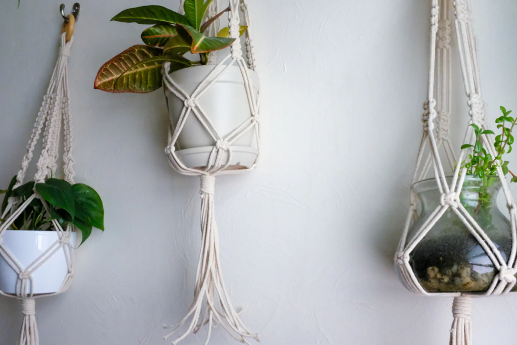 3 cream macrame plant holders filled with pots and green houseplants 