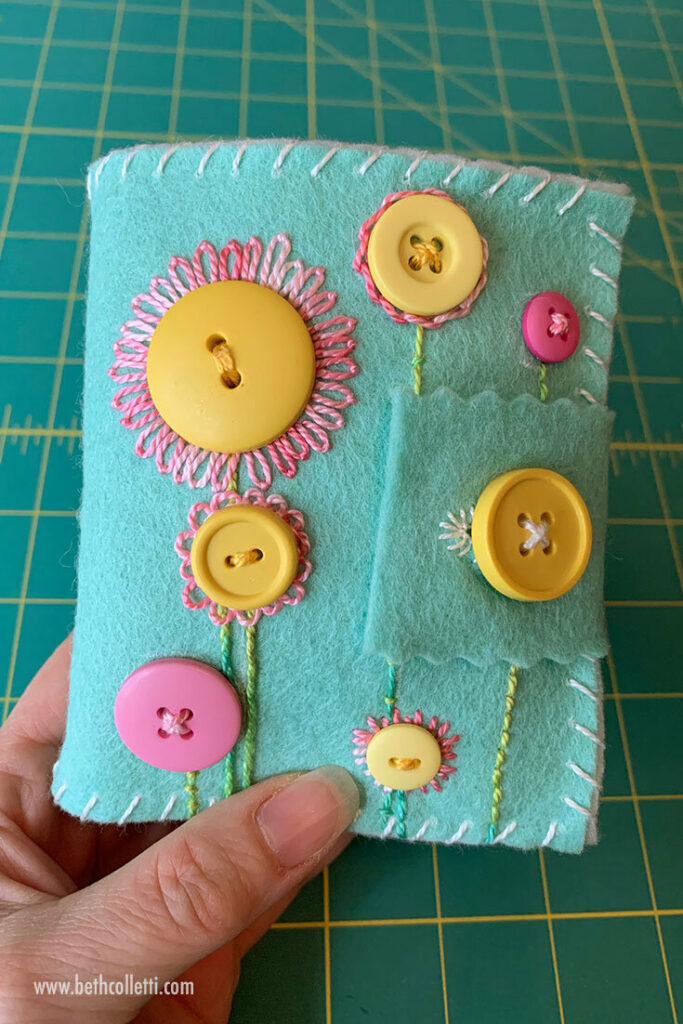 A felt and embroidered needlebook against an Olfa cutting mat background