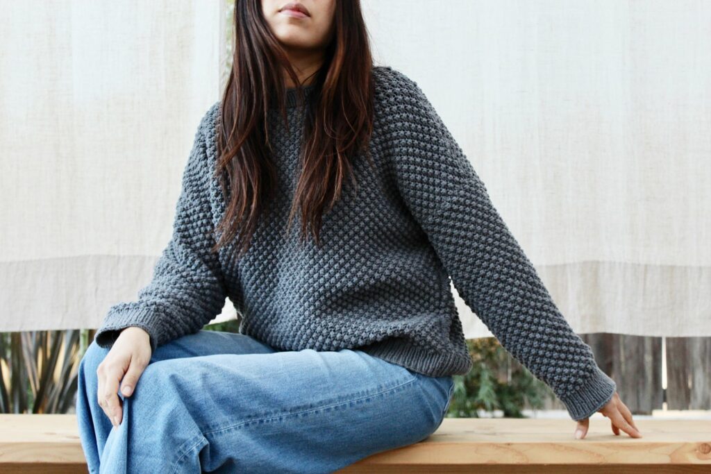 charcoal grey sweater on a woman wearing blue jeans and sitting on a wooden bench 