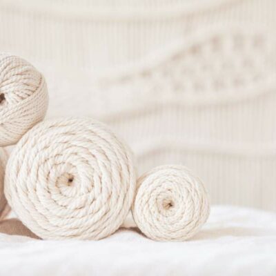 white macrame cord piled on a table, with a macrame wall hanging in the background