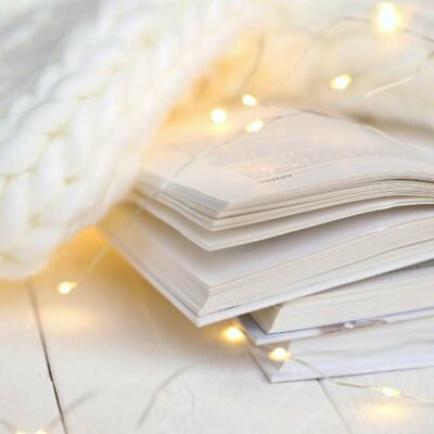 open books covered by a thick white knit blanket, fairy lights are woven throughout the scene