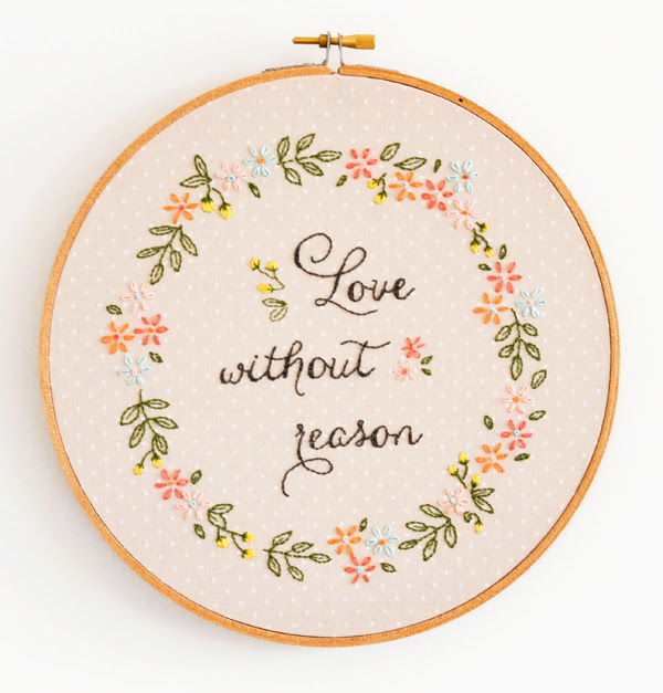 An embroidery piece in a hoop with a floral wreath and the text 'Love without reason'