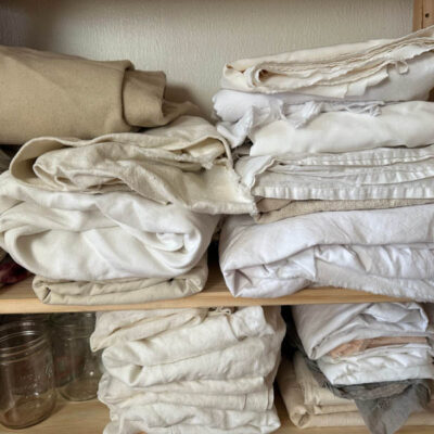 Pile of cream and white fabrics on a wooden shelf.