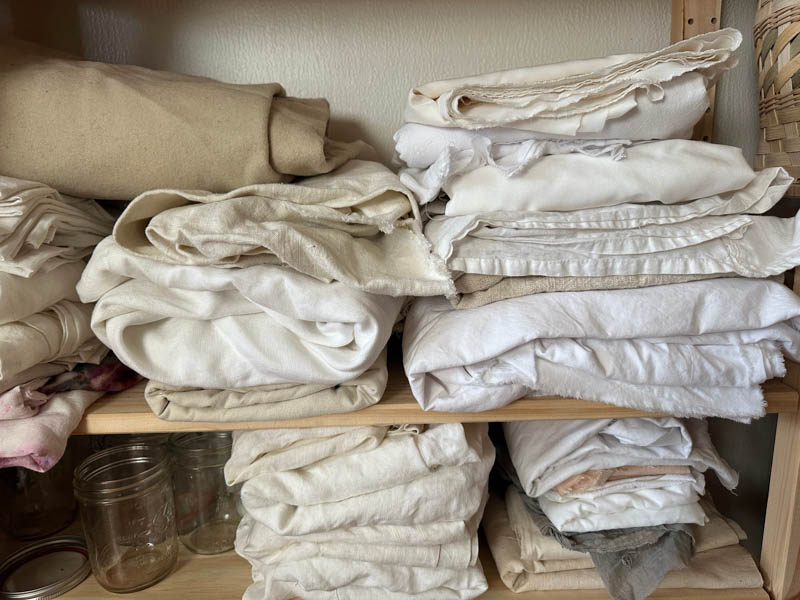 Pile of cream and white fabrics on a wooden shelf.