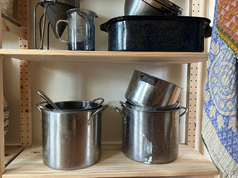 Stacks of stainless steel pots on a wooden shelf.