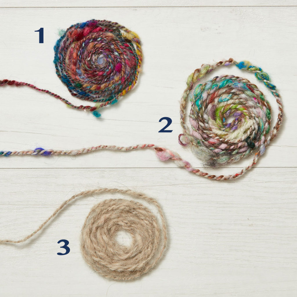 Spin off magazine yarn challenge, three different types of hand spun yarn are spiraled on a white board 