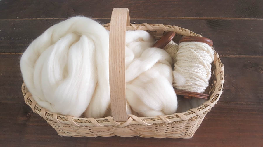 basket full of white wool roving with two bobbins of spun white yarn 