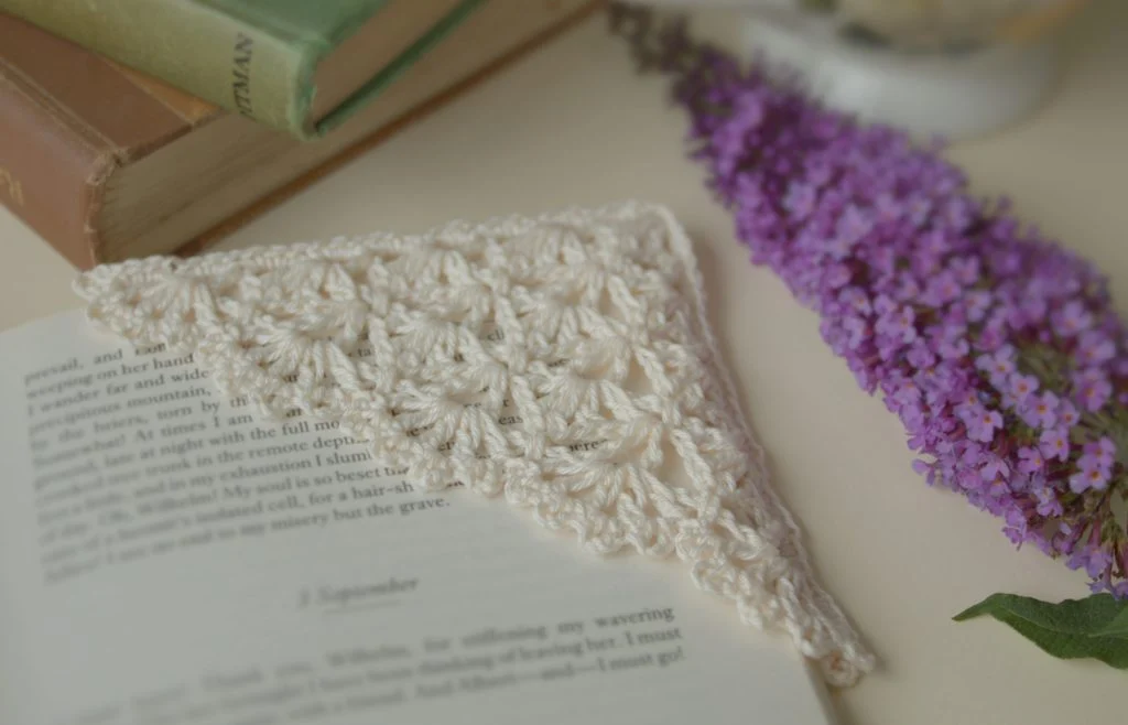 Blue Star Crochet corner bookmark in cream, sprig of butterfly bush in the background 