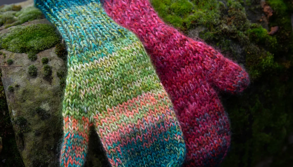 Brightly colored mittens on a moss covered log 