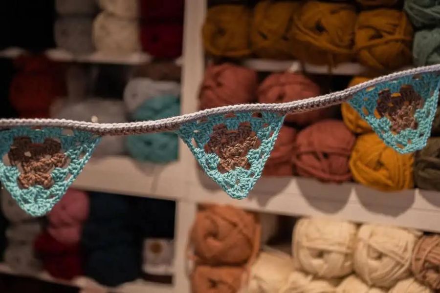 Turquoise and brown crochet bunting hanging in front of a wall of yarn 