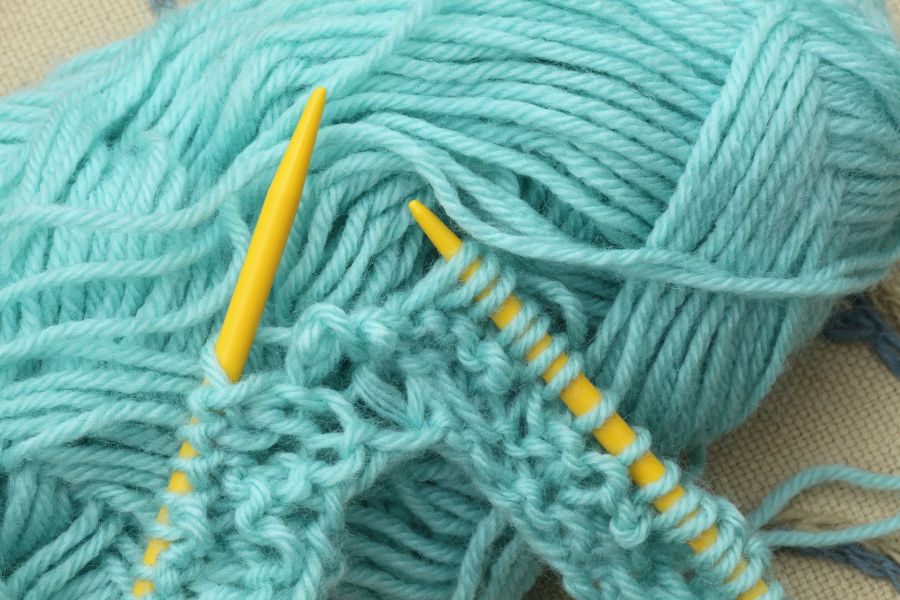 Turquoise skein of yarn, with yellow knitting needles in the process of knitting
